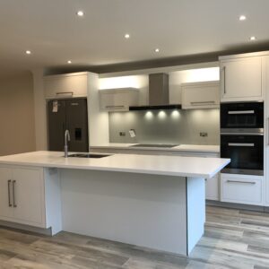 Modern kitchen renovation featuring a white central island, handleless cabinetry, integrated appliances, recessed ceiling lighting and warm wood flooring.