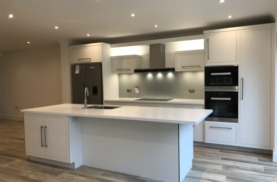 Modern kitchen renovation featuring a white central island, handleless cabinetry, integrated appliances, recessed ceiling lighting and warm wood flooring.