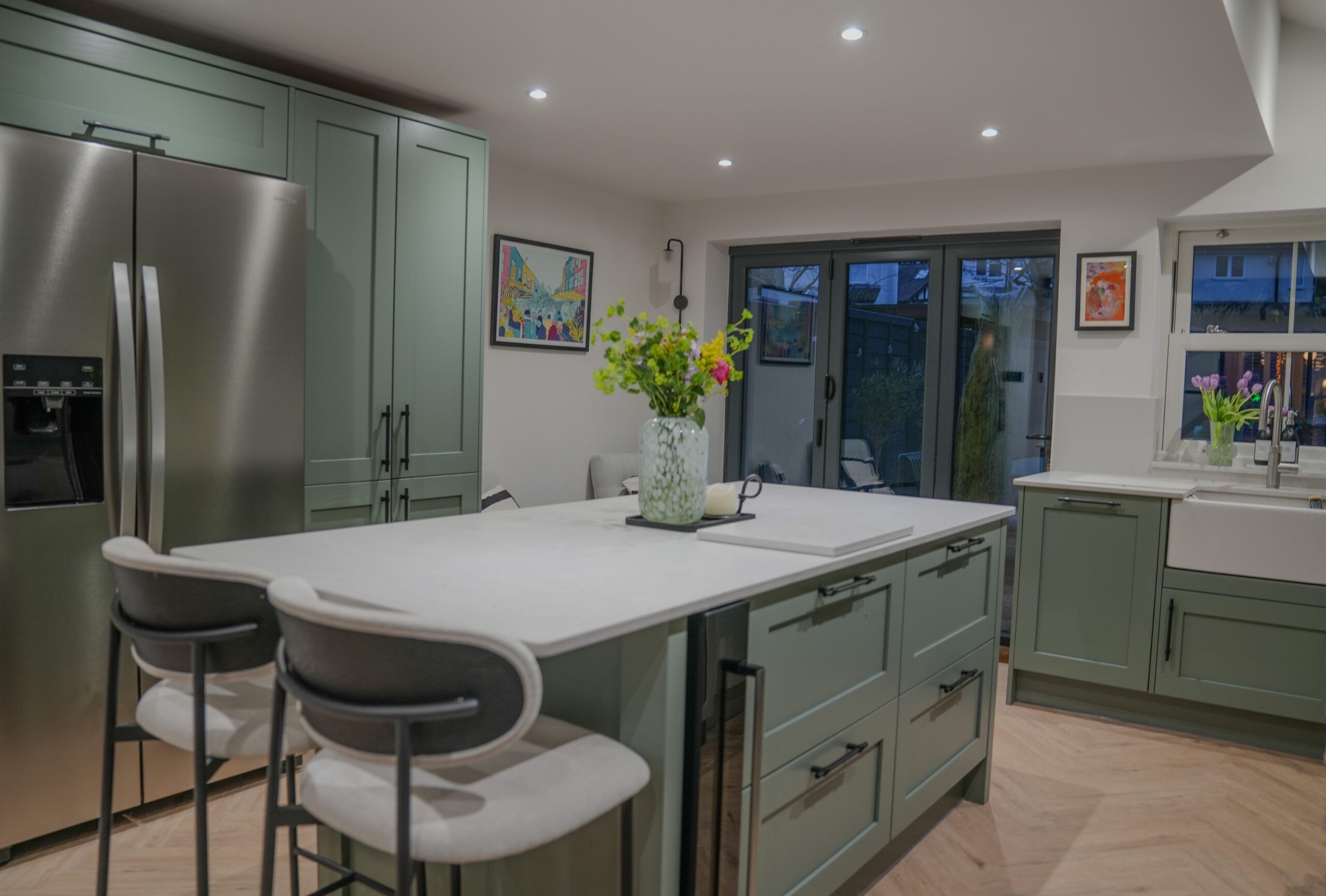 Modern sage green kitchen renovation featuring shaker-style cabinetry, a white island countertop, breakfast bar seating, stainless steel appliances and light herringbone flooring